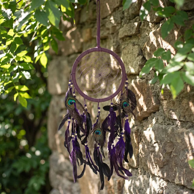 Purple feather dreamcatcher hanging outdoors on stone wall amidst greenery, showcasing soft natural morning light and detailed feathers.