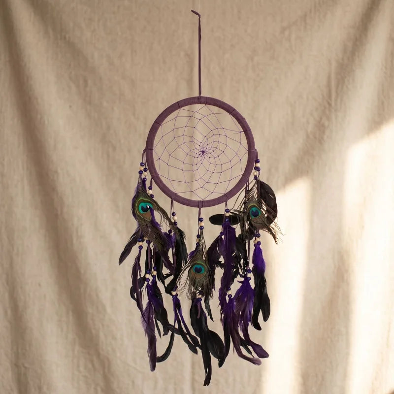 Close-up of purple feather dreamcatcher with peacock feathers and purple stitching against soft, textured tapestry backdrop.