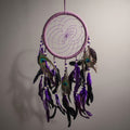 Studio image of purple feather dreamcatcher suspended in mid-air with diffused lighting accentuating stitching and layered feathers.