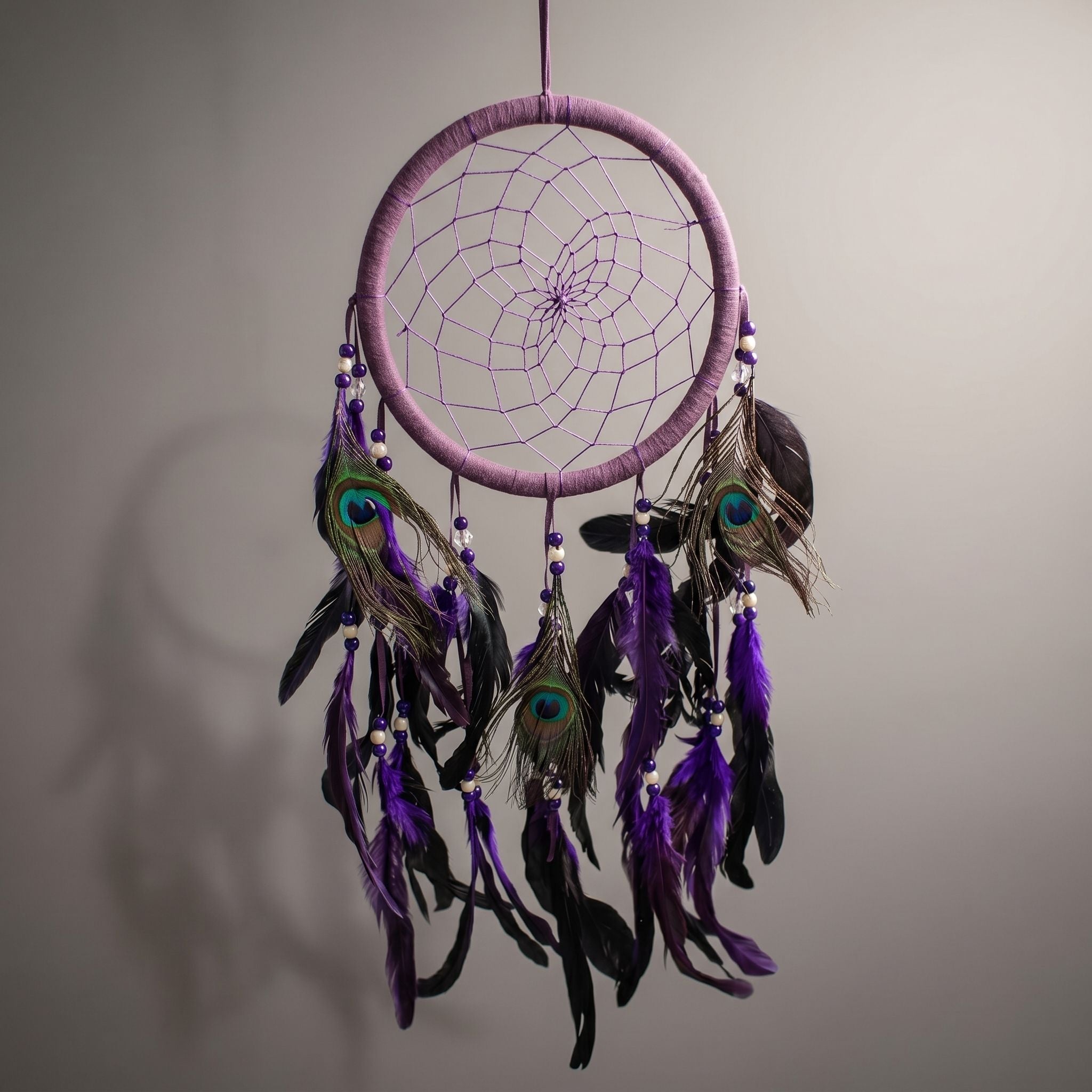 Studio image of purple feather dreamcatcher suspended in mid-air with diffused lighting accentuating stitching and layered feathers.